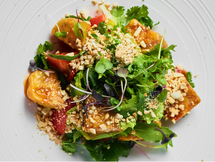 Gourmet vegetable salad topped with fresh microgreens, roasted golden vegetables, tomato wedges, and crushed nuts on a white plate
