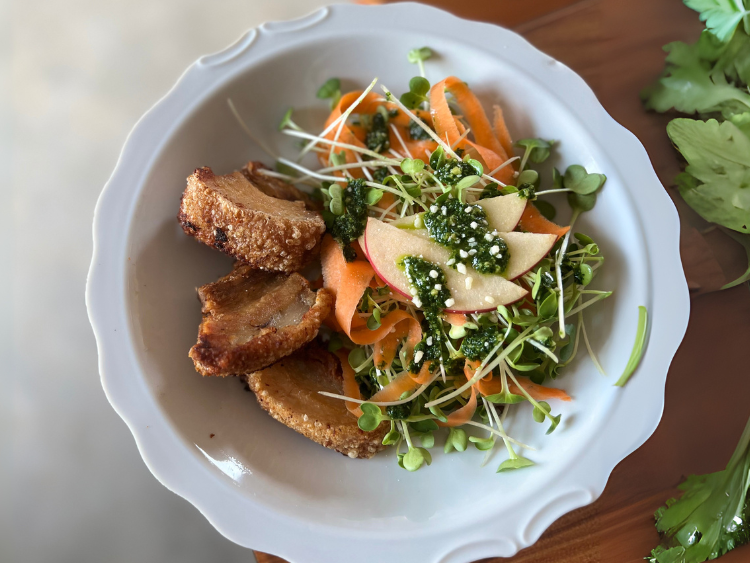 Microgreens salad with carrot ribbons, apple slices, herb dressing, and crispy pork belly slices served on a white plate — a fresh, healthy, and protein-packed dish.