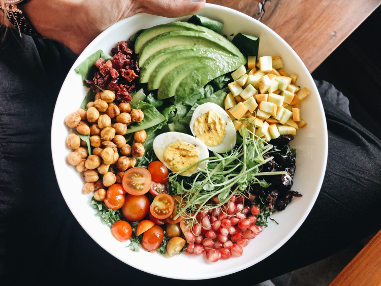 Power greens salad with avocado, hard-boiled egg, chickpeas, pea shoots, and fresh veggies in a white bowl