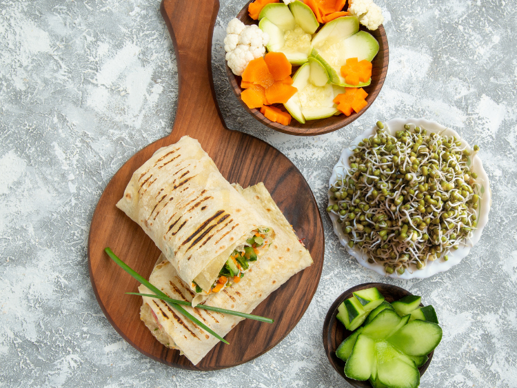 whole-grain-wrap-filled-with-hummus-mung-bean-sprouts-and-cucumber-served-with-sliced-vegetables-and-fresh-sprouts-on-wooden-board