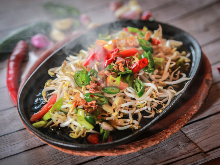 Hot sizzling plate of stir-fried bean sprouts with red and green chilies, scallions, and crispy shallots served on a cast-iron skillet — healthy Asian vegetable stir-fry.