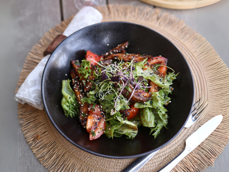 charred-vegetable-salad-with-sesame-seeds-microgreens-and-fresh-tomatoes-in-a-black-bowl