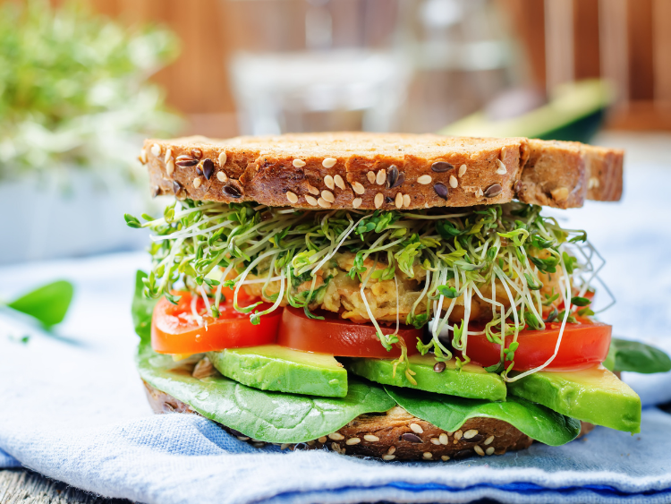 Whole grain rye sandwich layered with fresh spinach, sliced avocado, juicy tomato, crispy chickpea patty, and crunchy alfalfa sprouts, served as a healthy vegan power sandwich